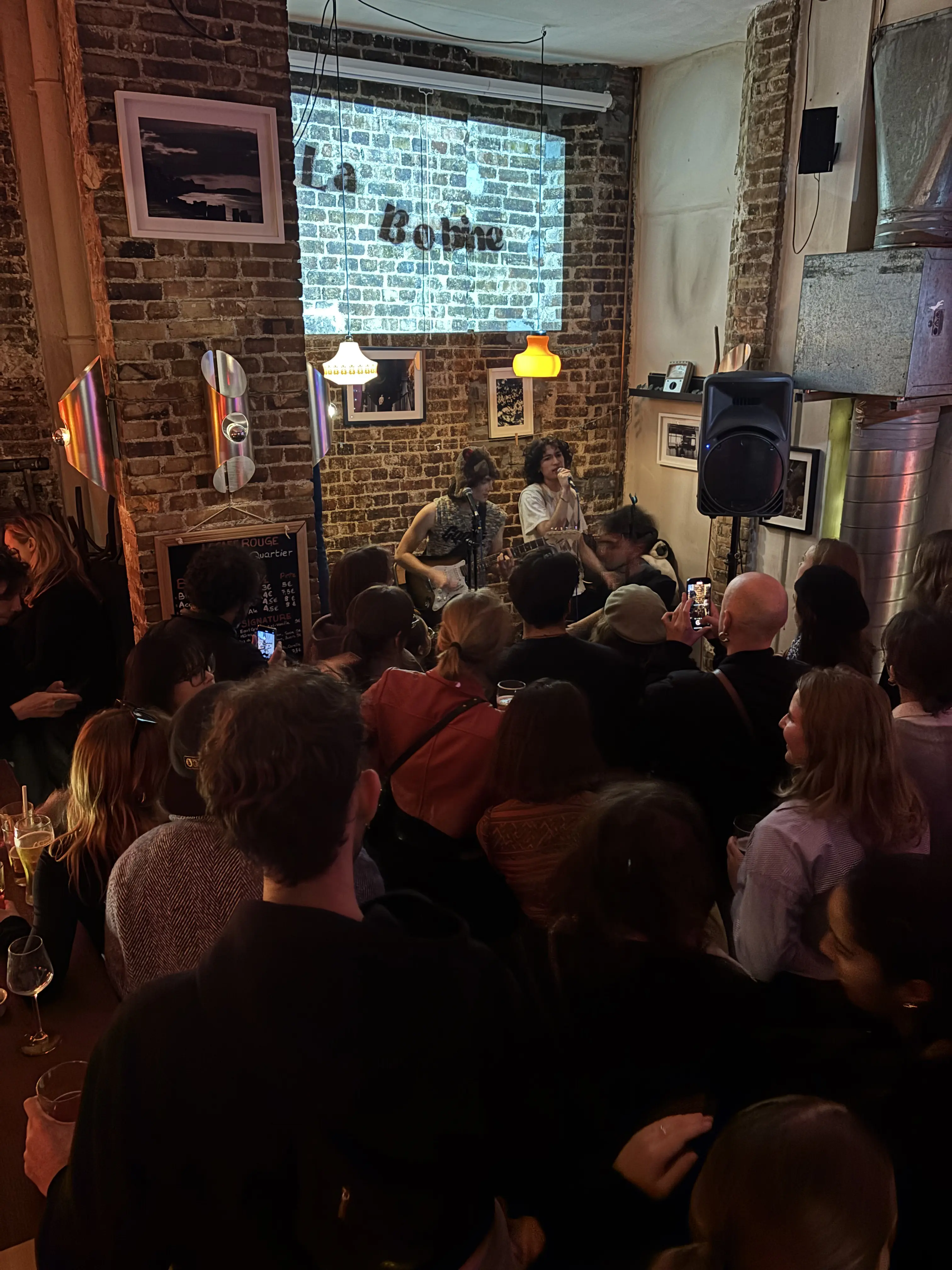 Public dense dans un bar culturel devant un concert, typique des concerts à Paris.