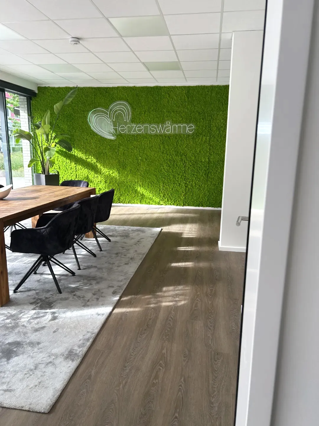 Besprechungsraum mit grüner Mooswand mit Logo und Schriftzug "Herzenswärme"