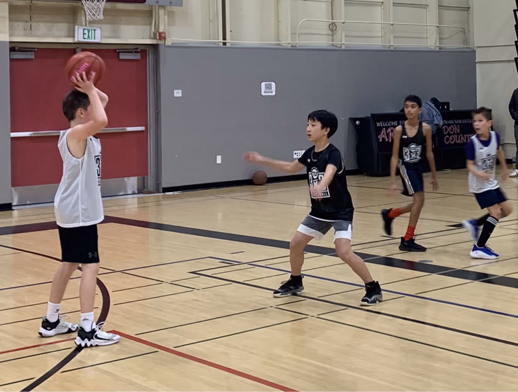Young boys playing basketball in a gym, one boy holding the ball overhead guarded by another player.