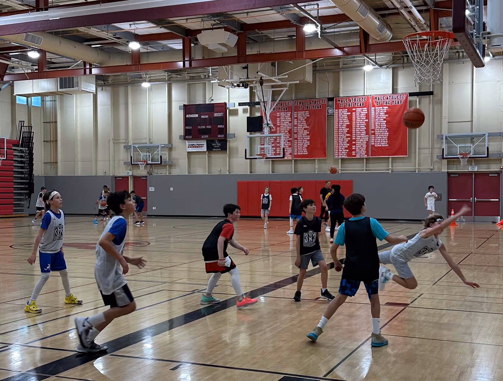 Four girls wearing sports jerseys huddled together with arms around each other on a gym floor.