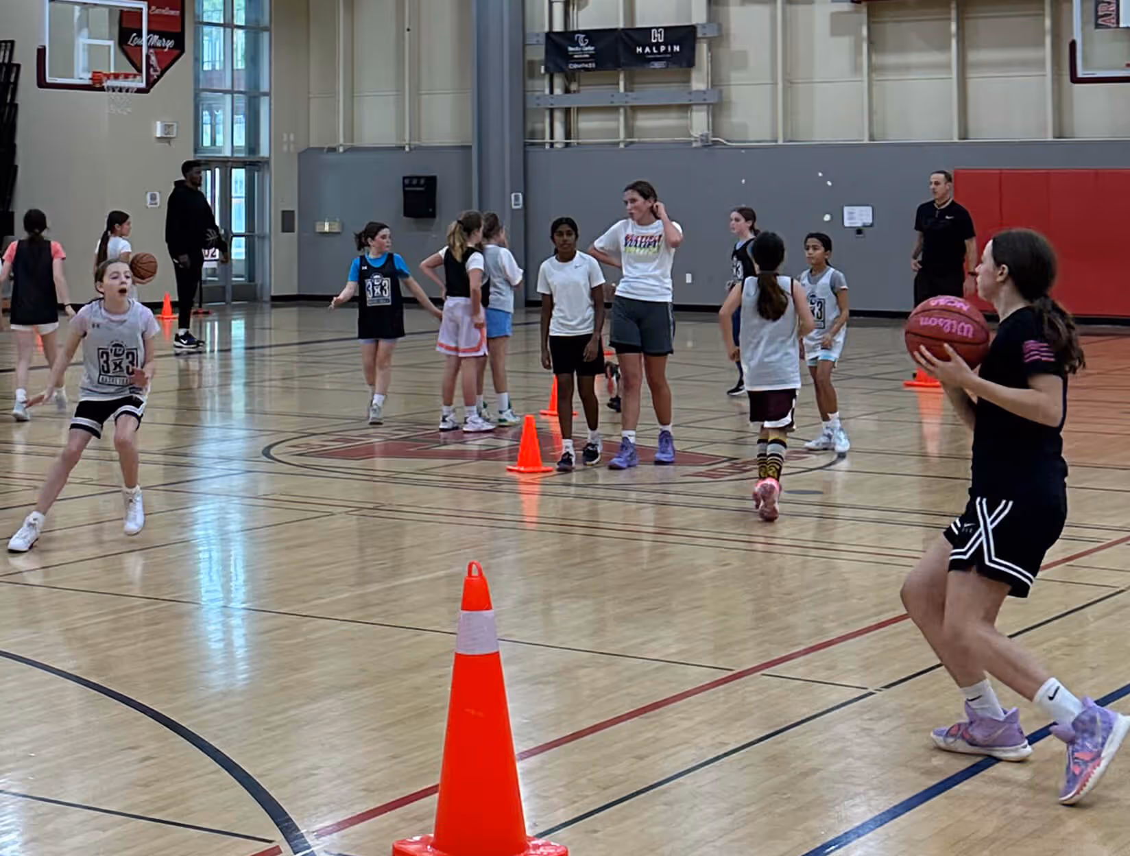 Children playing basketball in an indoor gym with red and black bleachers in the background.