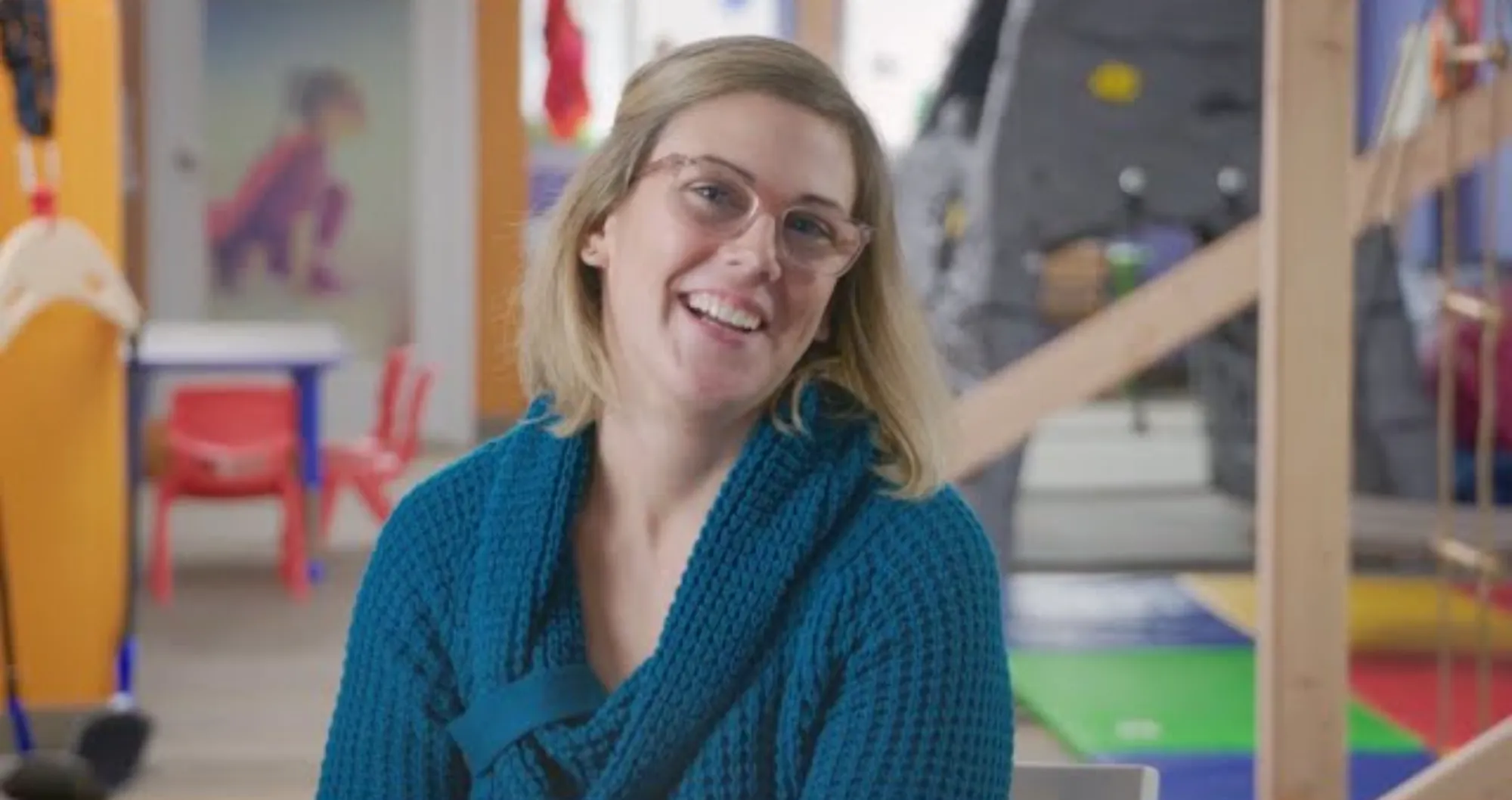 A pediatric occupational therapist sitting down smiling big at the camera