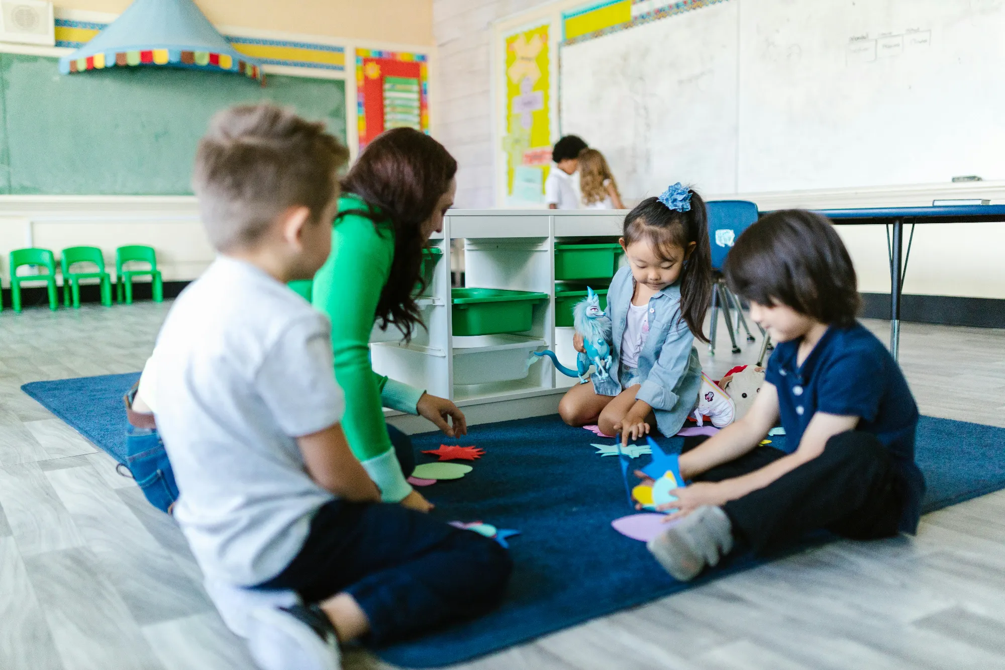 A teacher and three kids in a classroom, sitting together on the floor doing an activity
