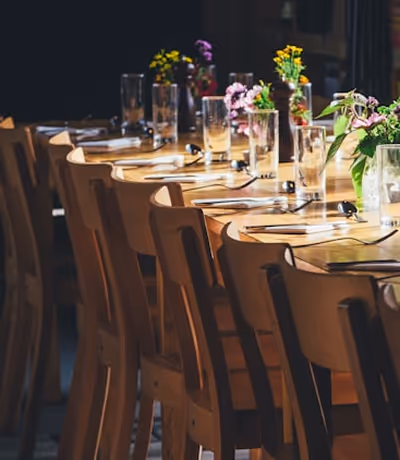 Table en bois dressée avec des verres, couverts et petits bouquets de fleurs diverses.