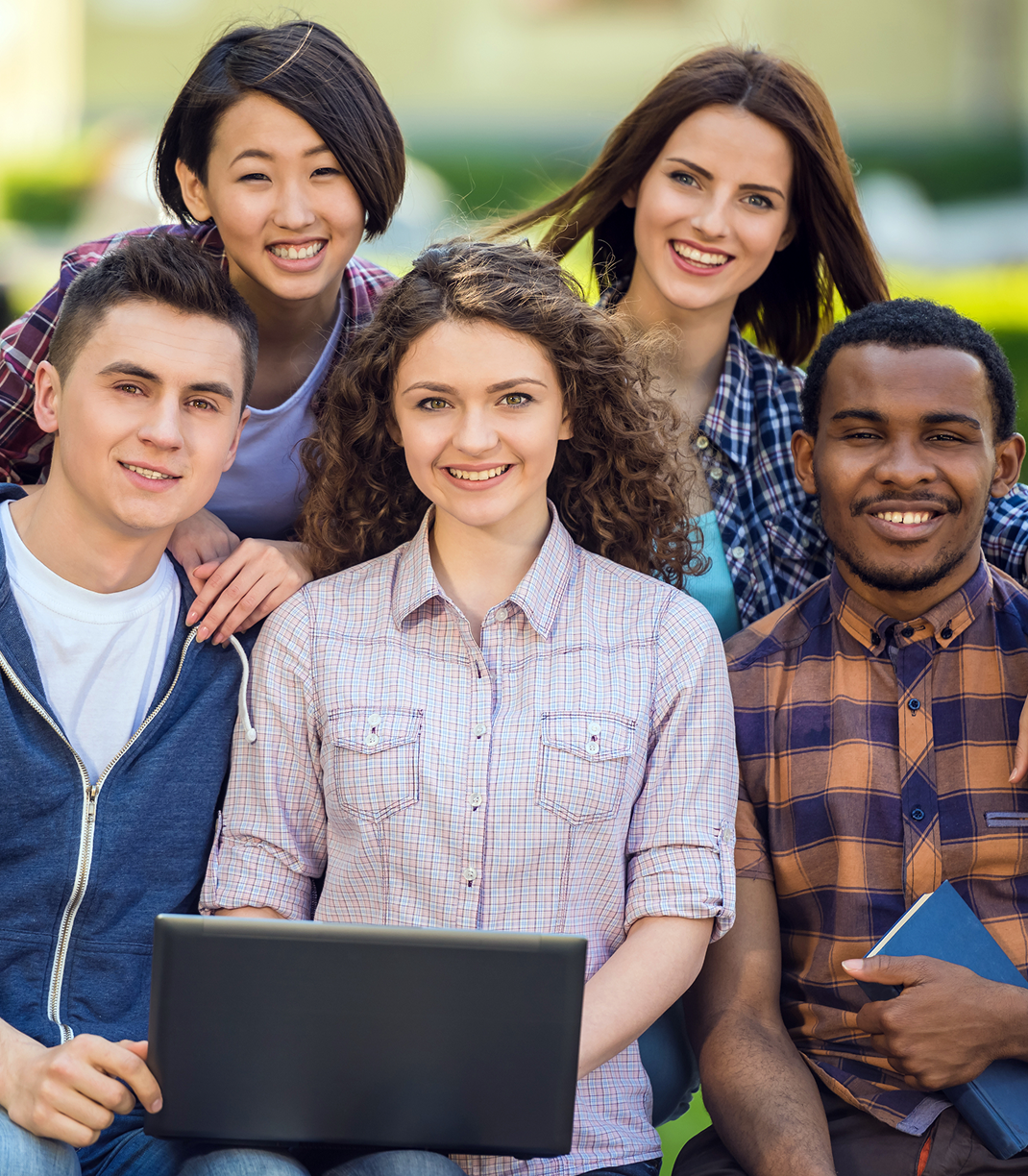 Five diverse global youth smiling together with a laptop outdoors, united through leadership and innovation