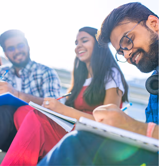 Three smiling youth writing notes outdoors, engaged in a funds-for-youth leadership learning program