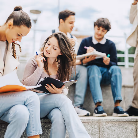 Group of young students writing and studying on campus steps, engaged in leadership development