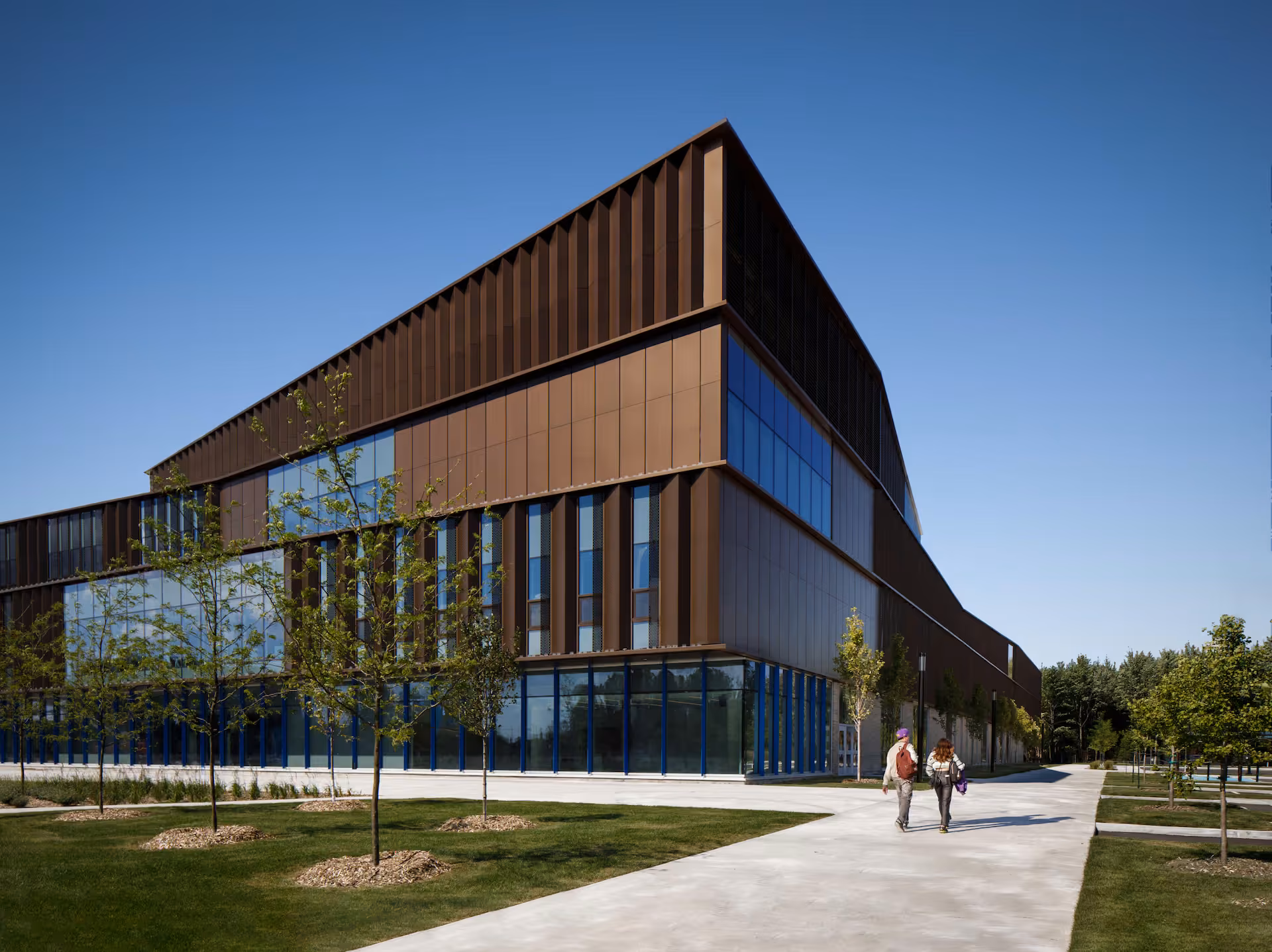 École secondaire du Bosquet : volume anguleux habillé de lames de bronze, grandes baies vitrées et parvis planté d'arbres.