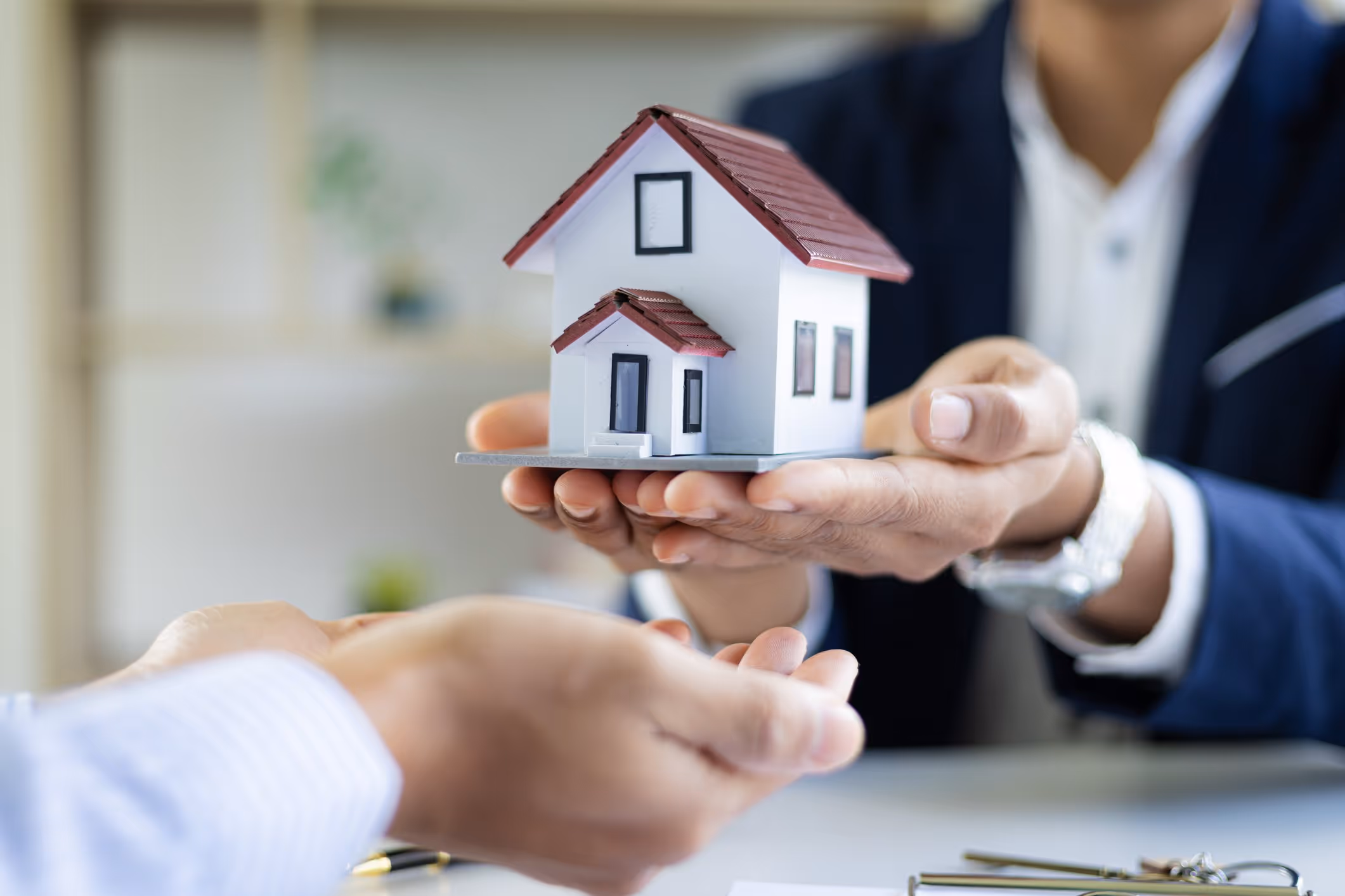 Geschäftsperson übergibt ein Modellhaus an eine andere Person, Symbol für Immobilienkauf oder -verkauf.