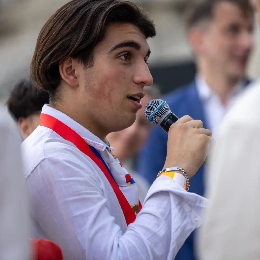 Jeune homme en chemise blanche parlant dans un microphone lors d'un événement.