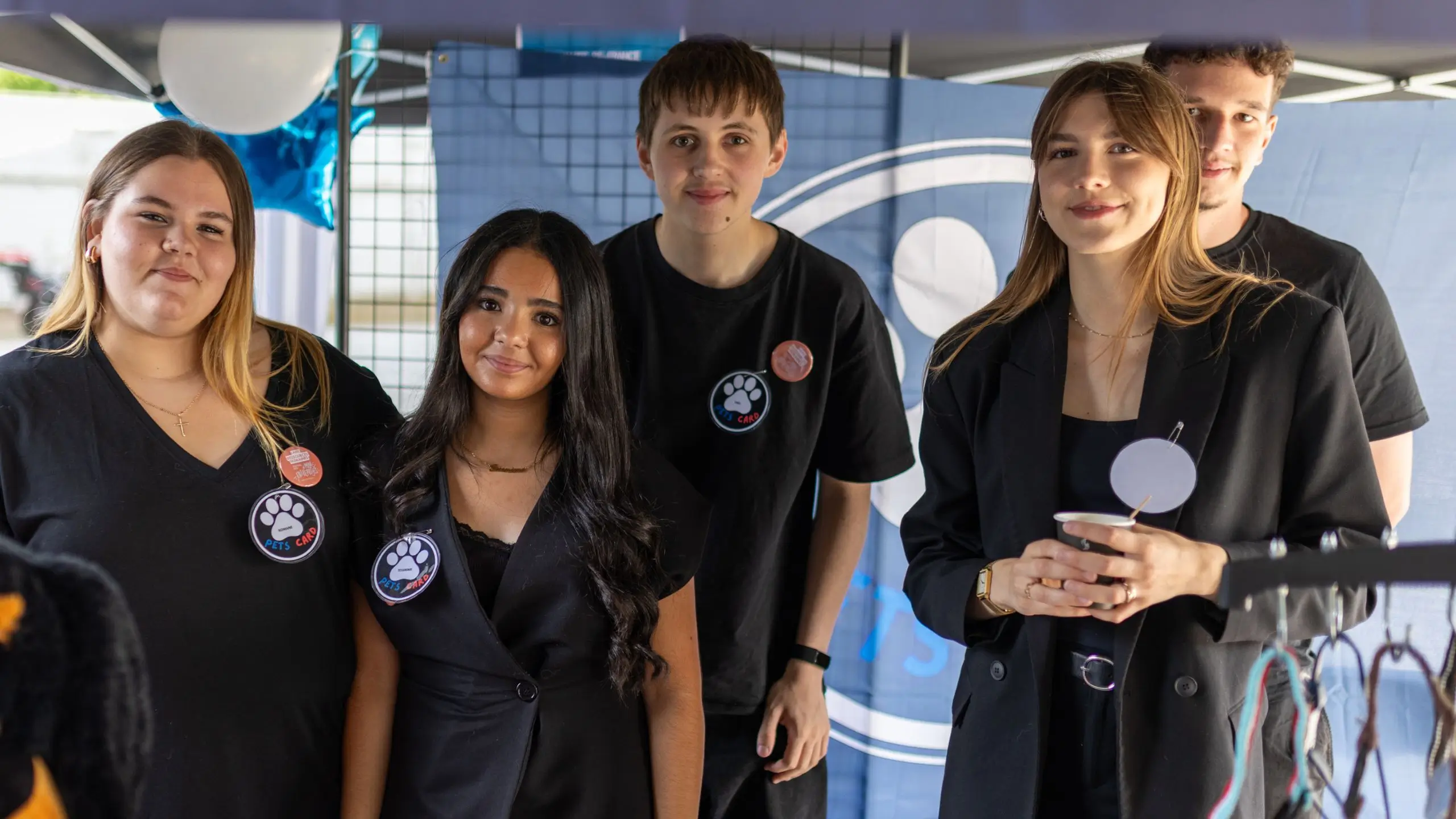 Groupe de cinq jeunes souriants portant des badges Pets Card lors d'un événement sous tente.