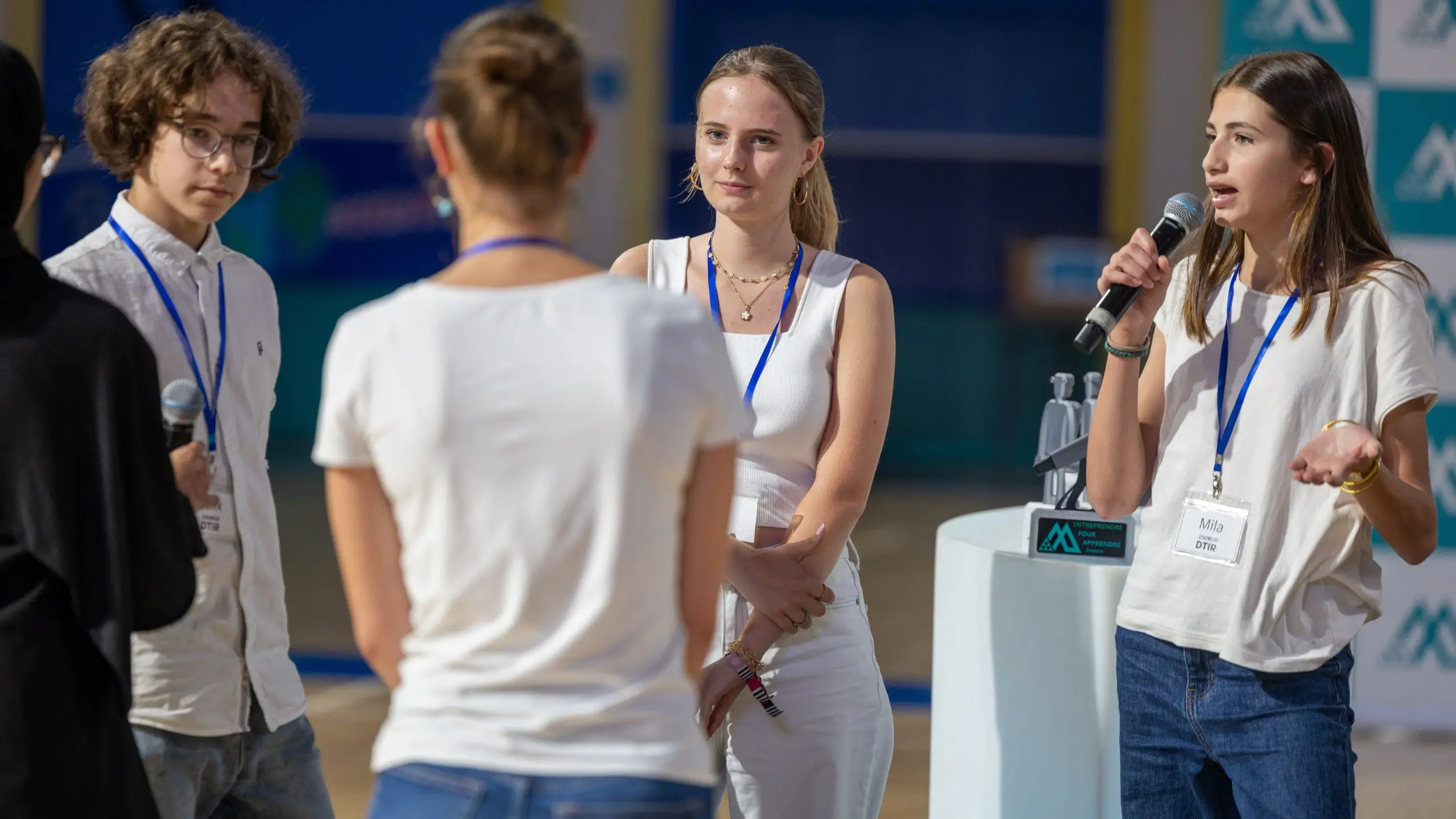 Quatre jeunes gens discutant dans un cadre professionnel, une fille parle au micro avec un badge autour du cou.