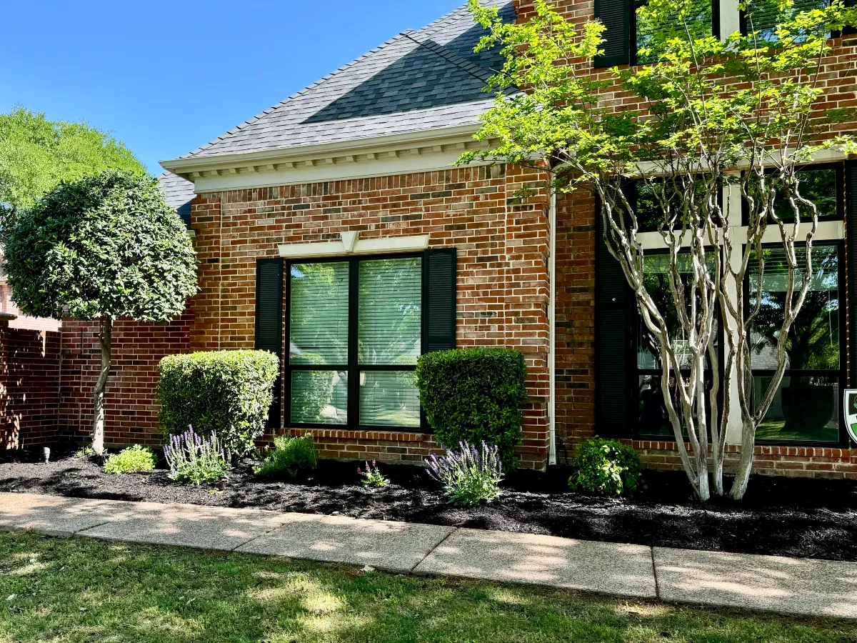 Residential landscaping with trimmed shrubs and flower beds around a brick home