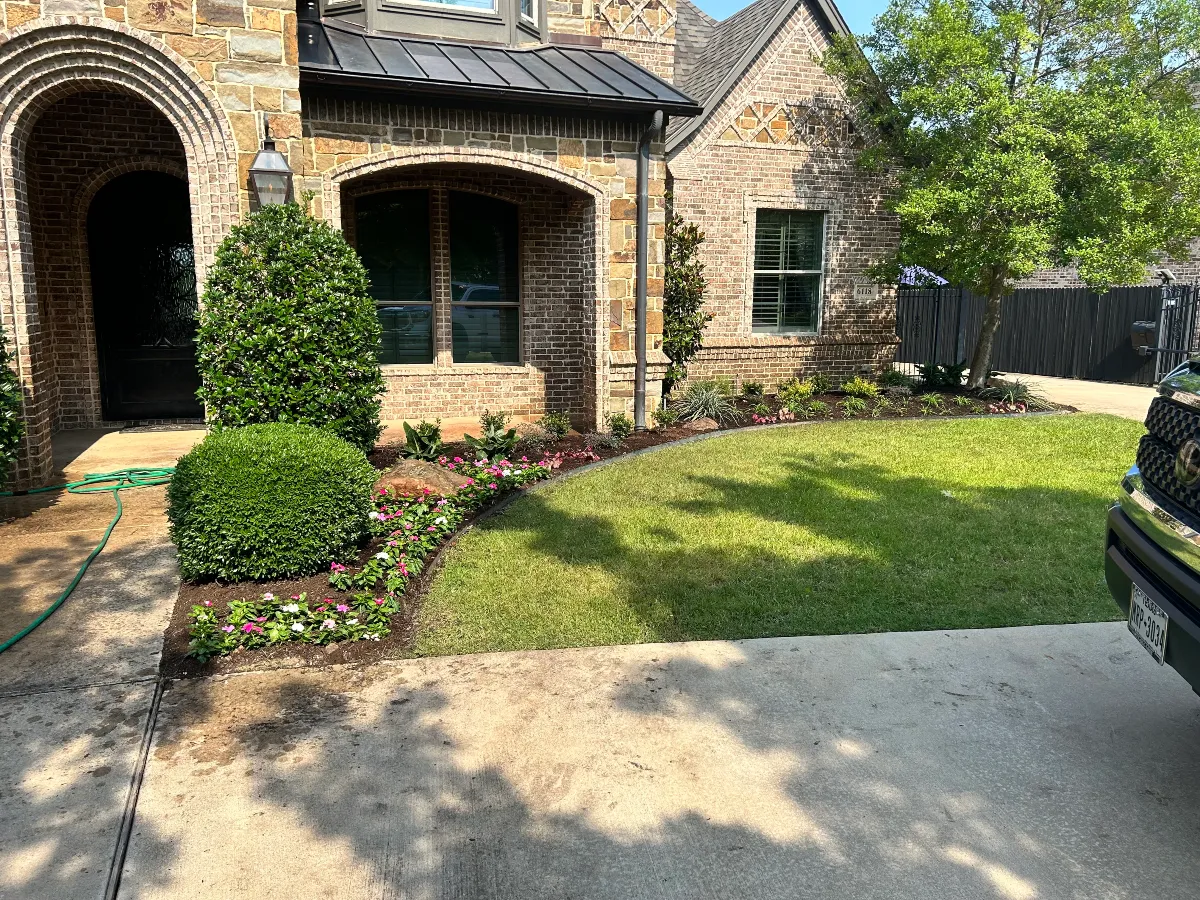 Manicured front yard with trimmed shrubs, flowers, and green lawn beside a stone home