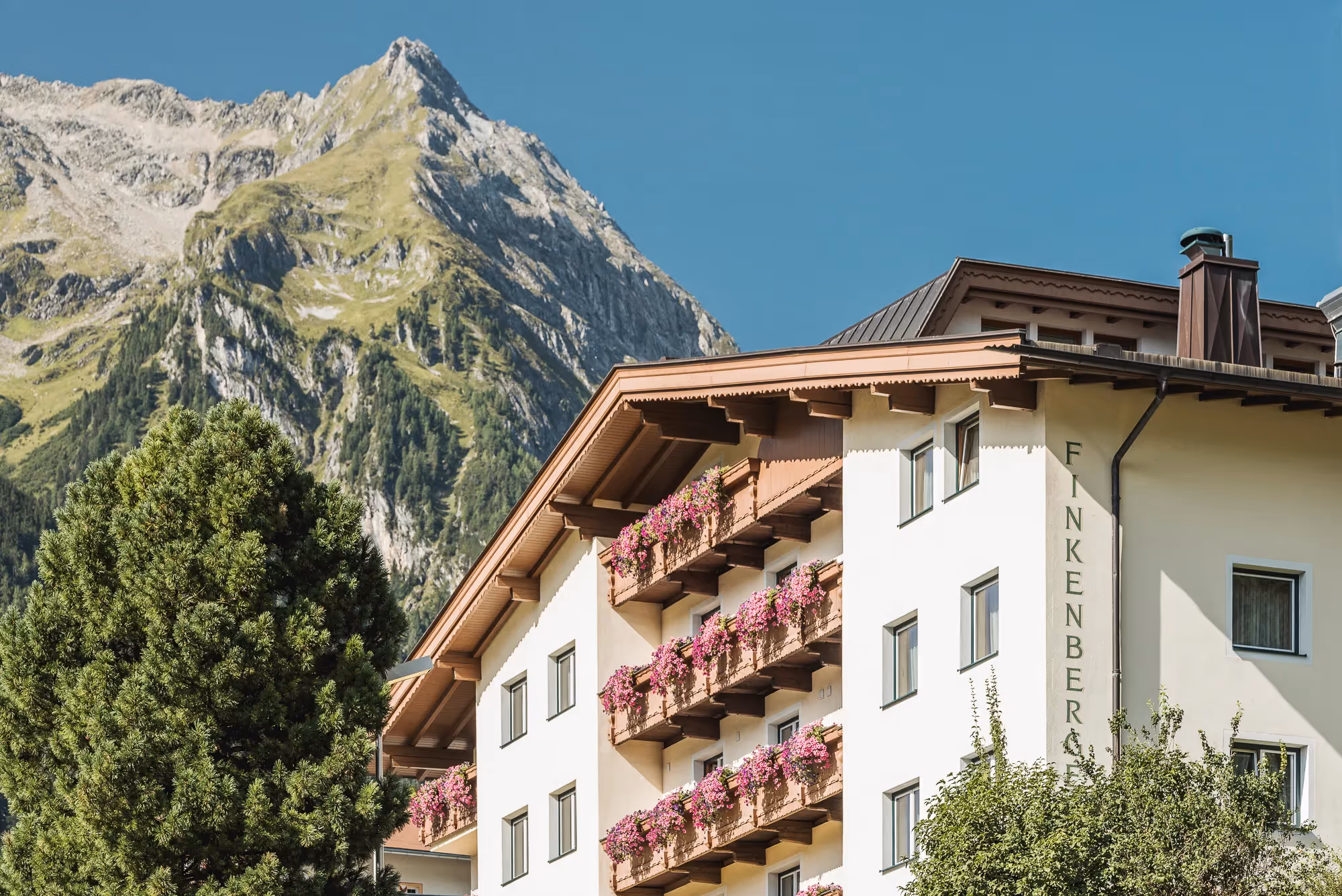 Alpenhotel Finkenberger Hof mit blumengeschmückten Balkonen vor einem Bergpanorama bei klarem Himmel.