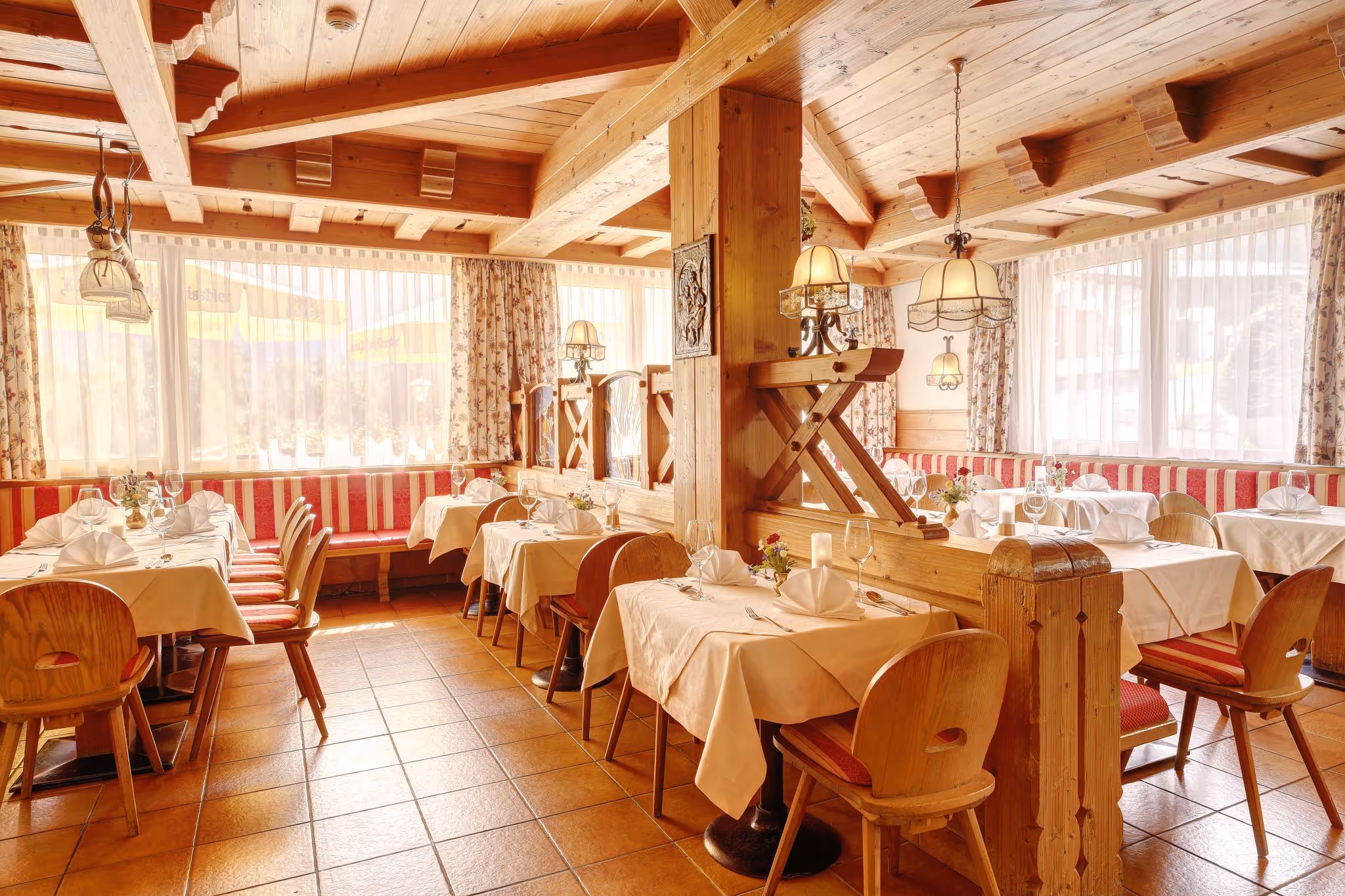 Gemütlicher Frühstücksraum mit rot gemusterten Sitzbänken, gedeckten Tischen und Buffet mit Kaffee- und Saftspendern.