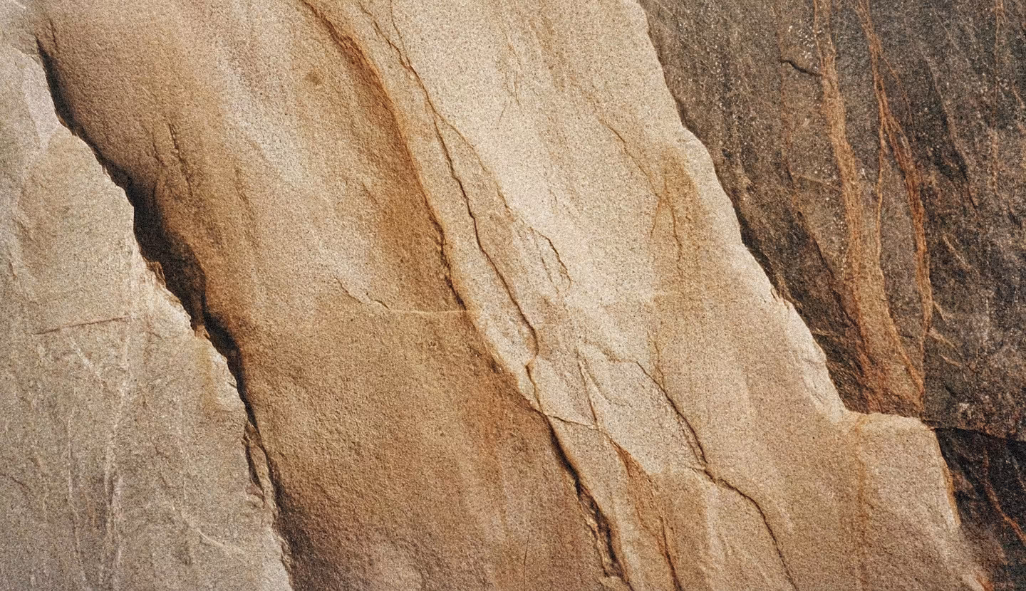 Close-up of rough, layered rock surface with vertical cracks and varying shades of beige and brown.