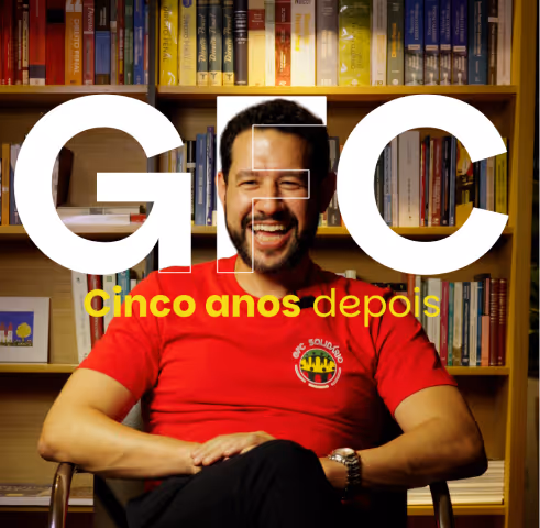 Smiling man with beard wearing a red GFC Solidário t-shirt sitting in front of a bookshelf, with overlaid text 'GFC cinco anos depois'.