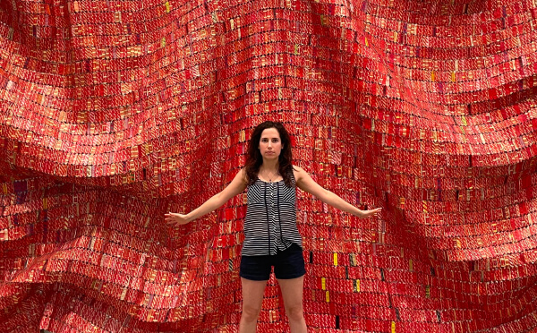 The architect, Anna Currant, standing in front of a red patterned tapestry.