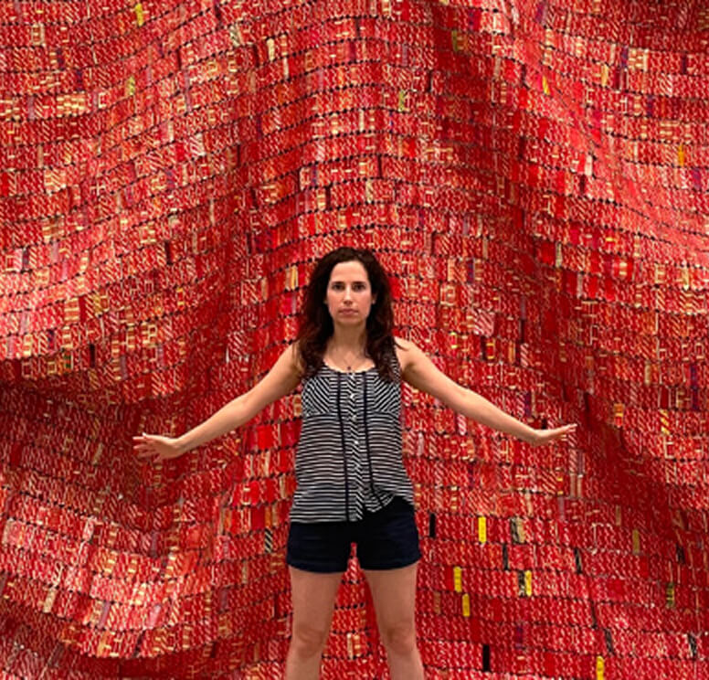 The architect, Anna Currant, standing in front of a red patterned tapestry.
