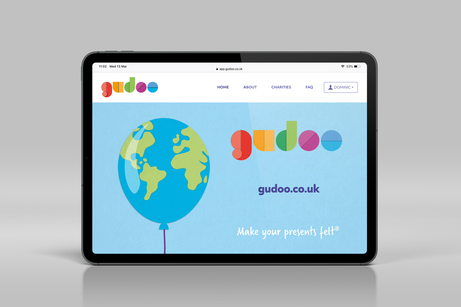 Tablet displaying gudoo.co.uk homepage with colourful logo, blue balloon with world map, and tagline 'Make your presents felt'.