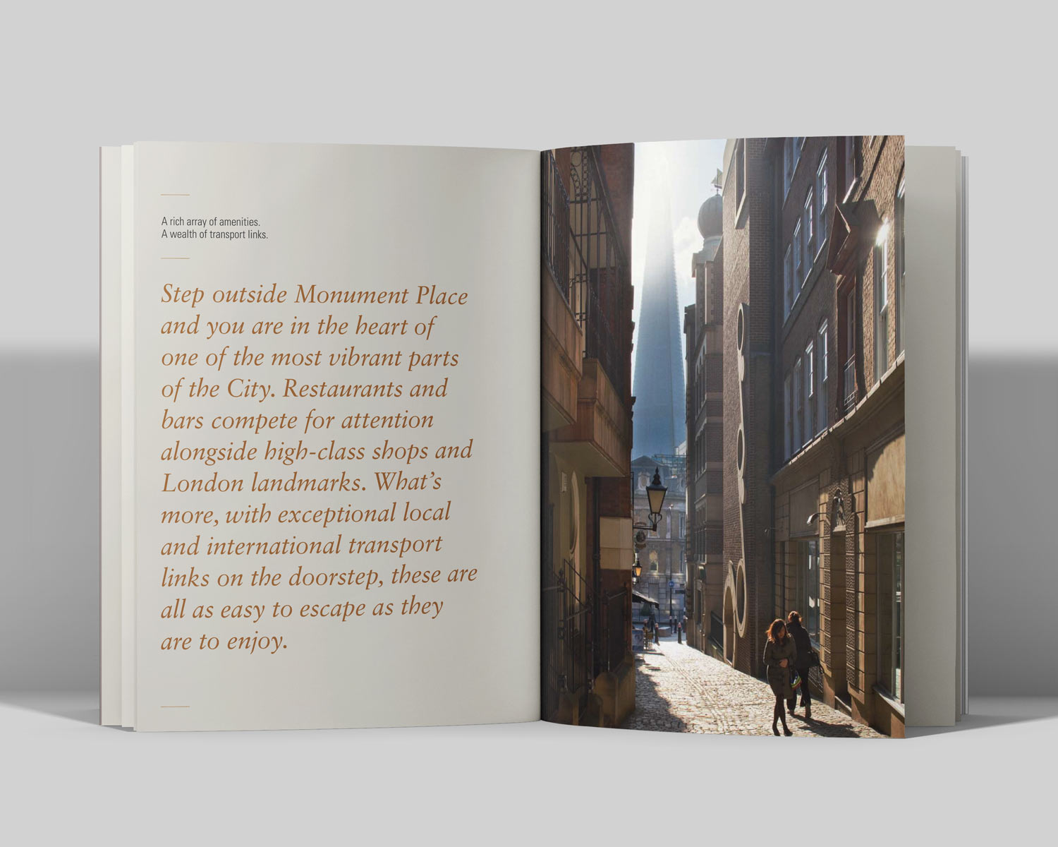 Open book showing a page with text about Monument Place and a photo of a sunlit cobblestone street in London with people walking and The Shard visible in the background.