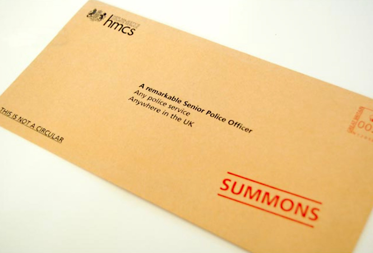 Close-up of a brown envelope labeled 'SUMMONS' addressed to a senior police officer from HM Courts Service.