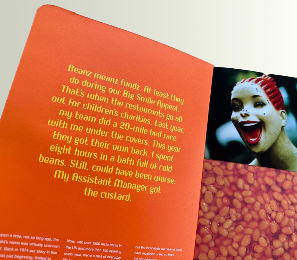 Open book showing text about a charity bed race event and a photo of a laughing statue with red hair.