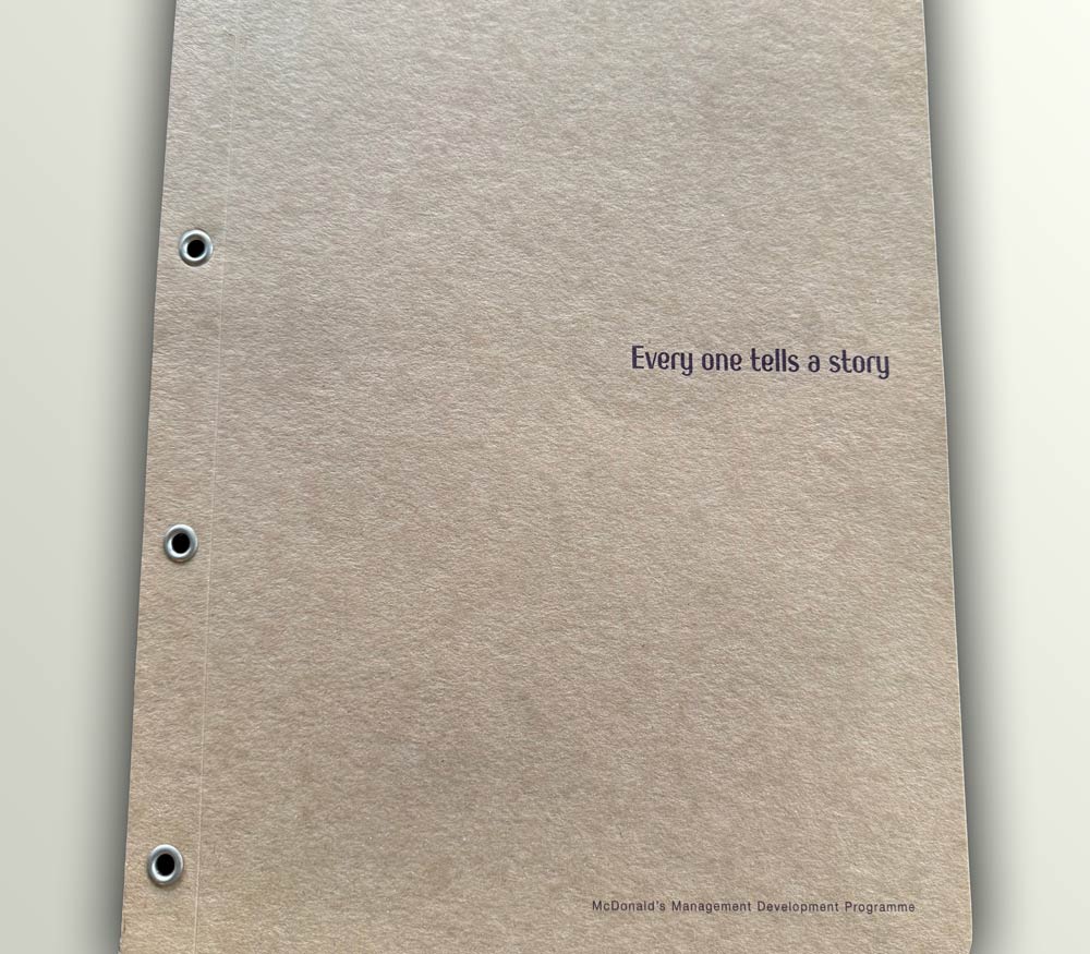 Craft board folder with the text 'Every one tells a story' and 'McDonald's Management Development Programme' printed on it.