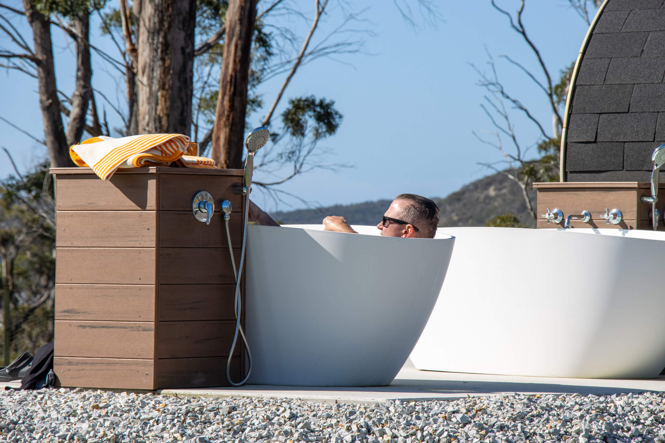 Young couple relaxing together in an outdoor bathtub at sunset surrounded by trees and nature.