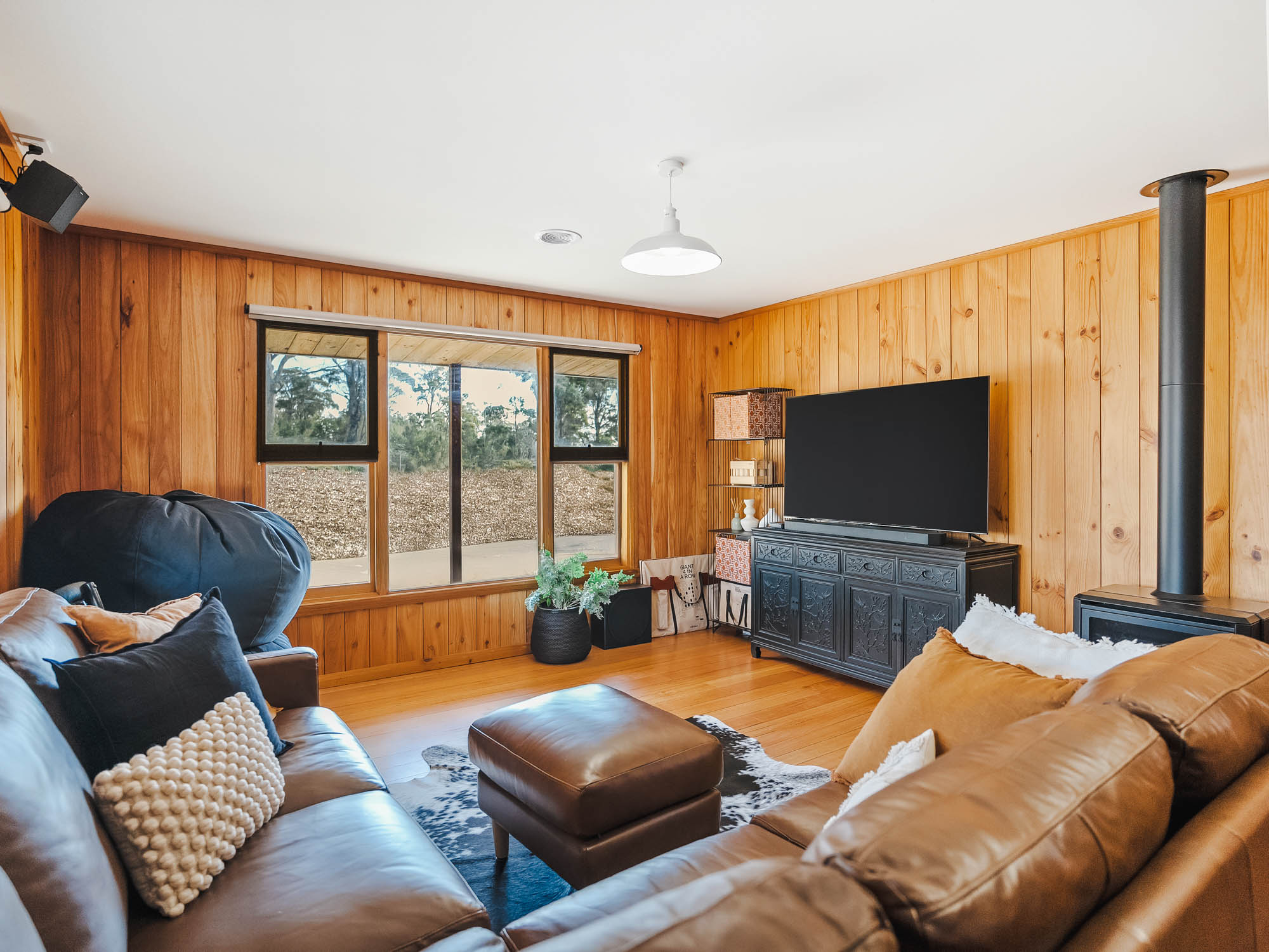 Charcuterie board on a gray wooden picnic table with assorted cheeses, crackers, grapes, cured meats, popcorn, dips, breadsticks, and a bottle of red wine with two glasses.