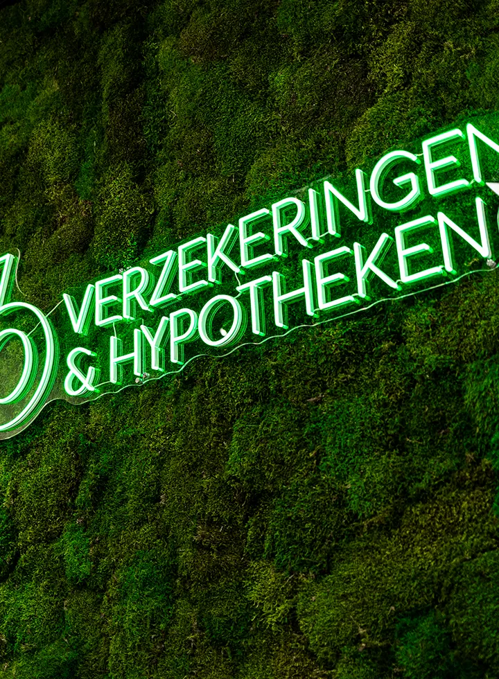 Neonlichtbord met de tekst 'Verzekeringen & Hypotheken' tegen een groene mosmuur.
