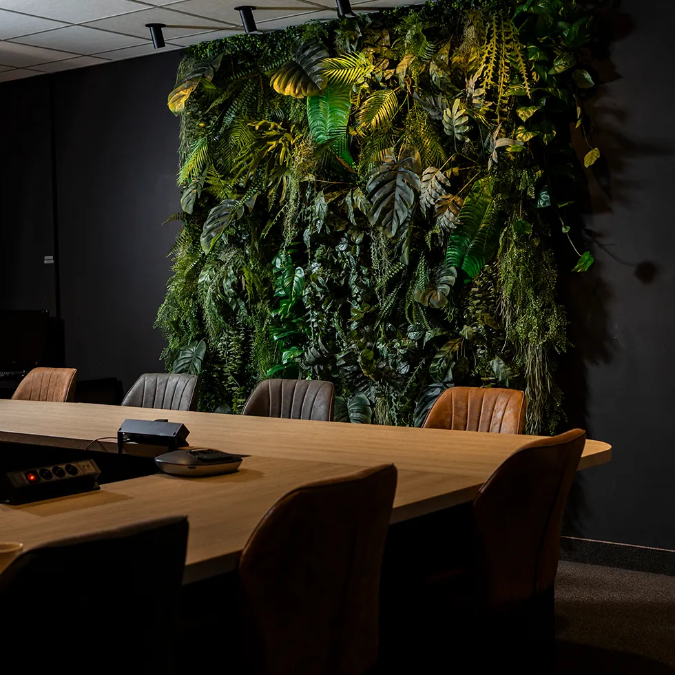 Vergaderruimte met een houten tafel, leren stoelen en een groene plantenmuur aan de zwarte wand.