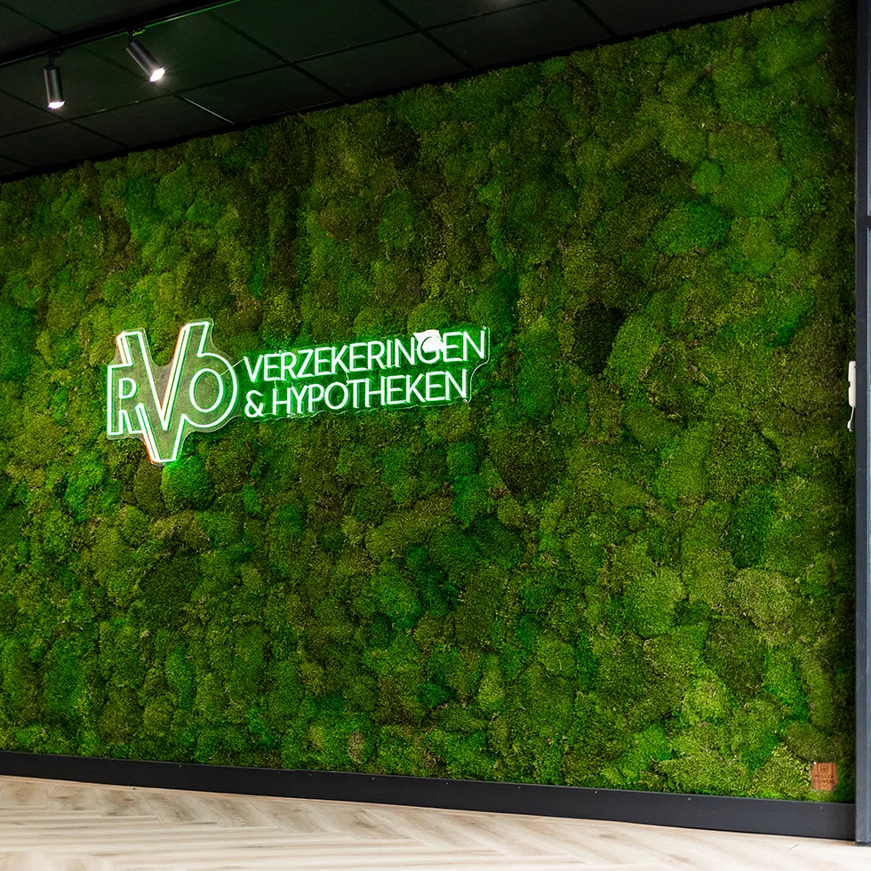 Groene mosmuur met verlicht bord met tekst 'RVO Verzekeringen & Hypotheken' in een moderne kantoorruimte.