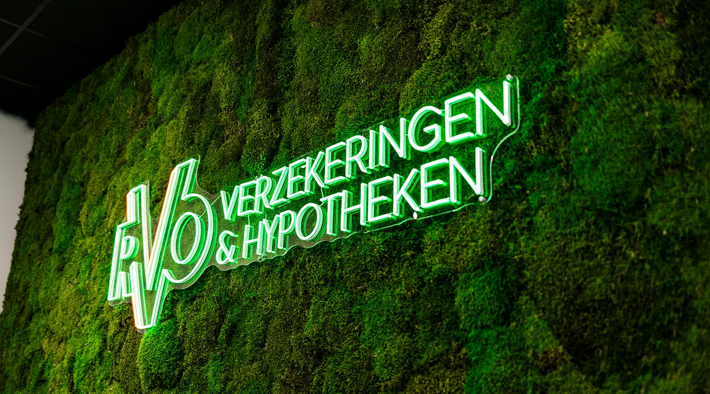 Neonverlichting met de tekst 'RV6 Verzekeringen & Hypotheken' op een groene moswand.
