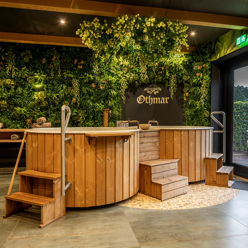 Houten spa-bad met traptreden vooraan en groene moswand met verlichting en het woord Othmar erop.