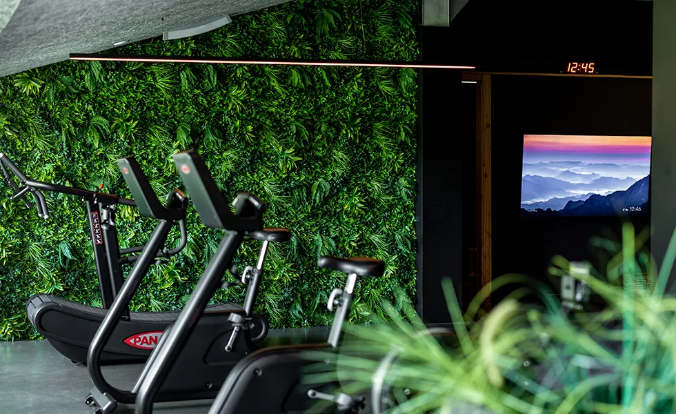 Sportschool met hometrainers voor een groene muur van planten en een televisie aan de muur met berglandschap.