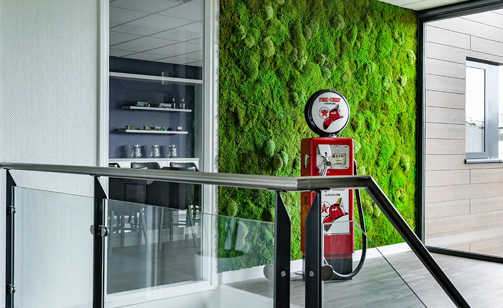 Rode vintage benzinepomp met Fire-Chief logo staat naast een groene mosmuur in een moderne ruimte met glazen hek en een zitkamer zichtbaar door een glaswand.