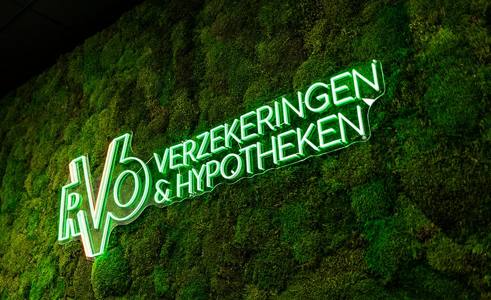 Groene neon verlichting tekst 'RV6 VERZEKERINGEN & HYPOTHEKEN' op een muur bedekt met mos