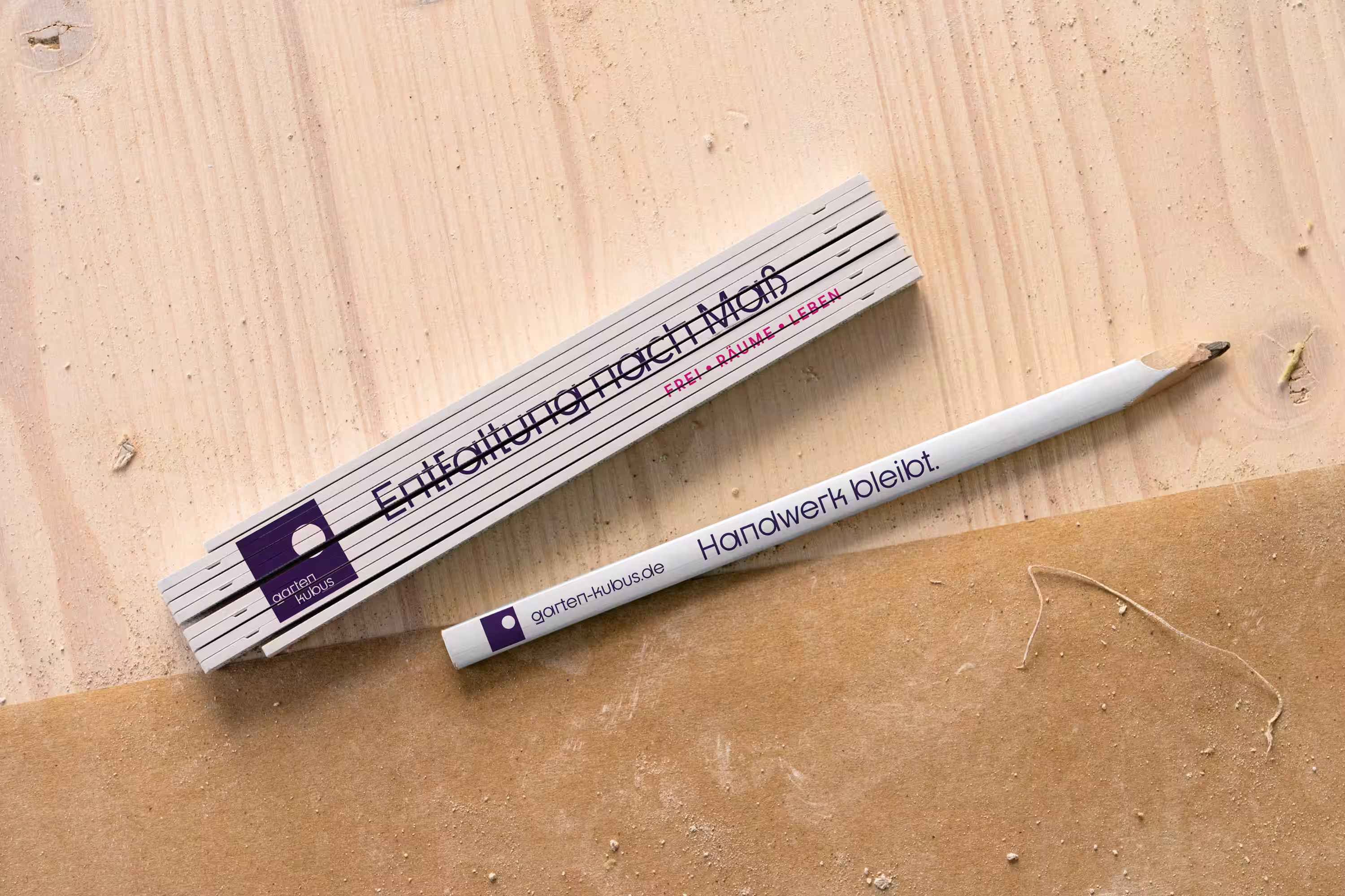 Garten Kubus: Merchandise-Artikel Zollstock und Bleistift mit Logo auf Holzplatte