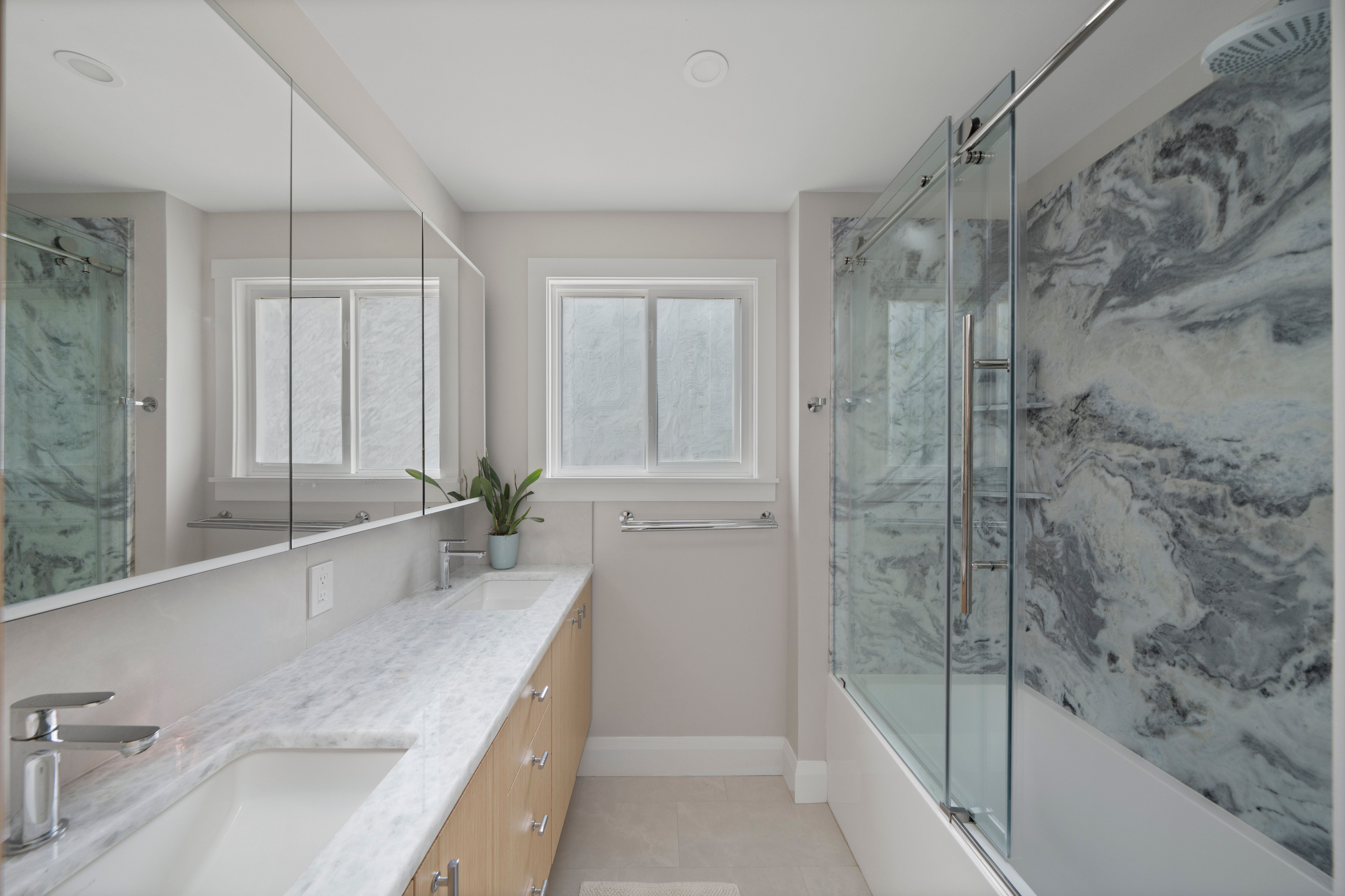Calm white and cream tones of the bathroom set off the dramatic quartzite countertop and marble shower surround.