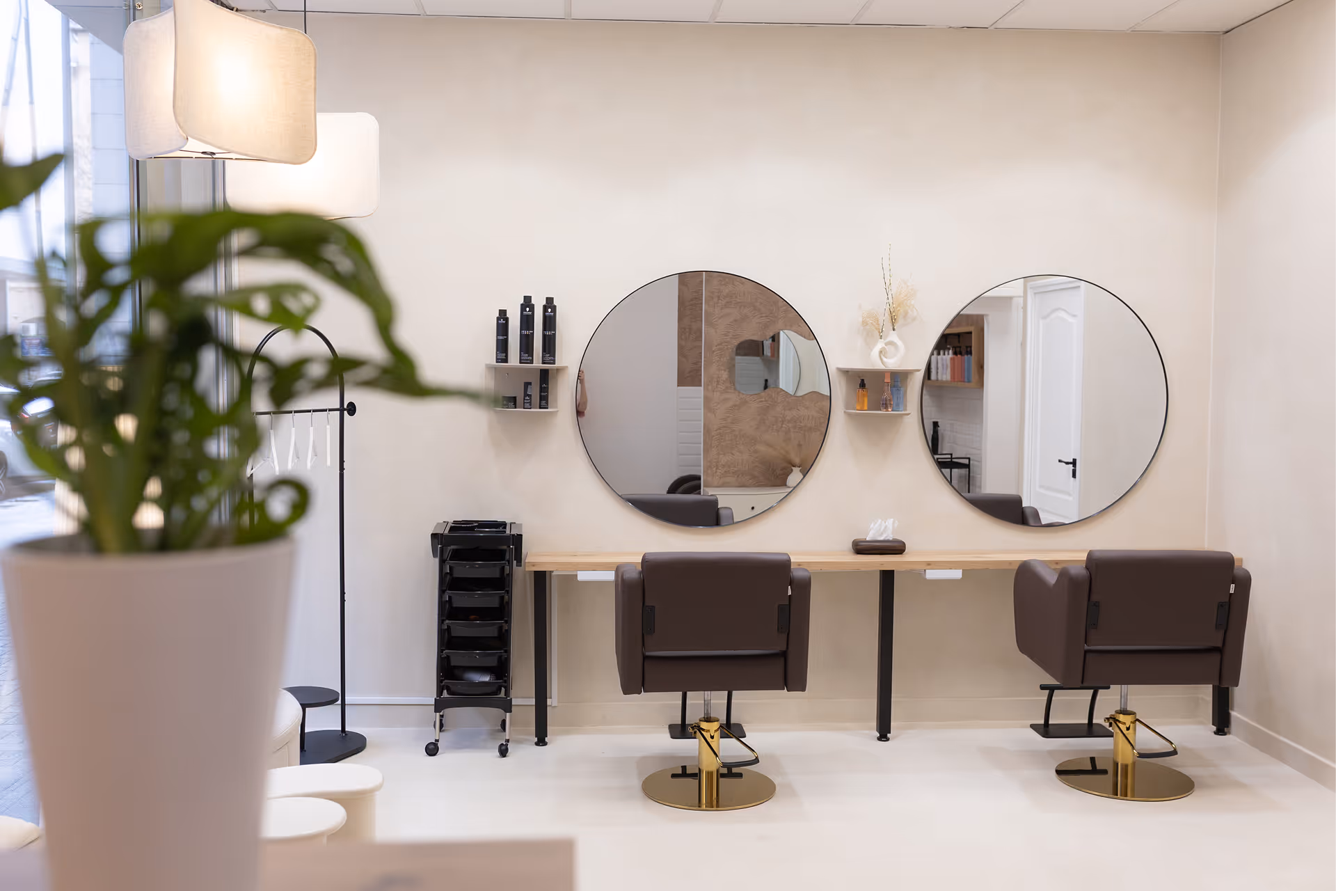Minimalista hajszalon belső tér két barna szalon székkel, kör alakú tükrökkel és polcokkal, amelyeken hajápolási termékek vannak.