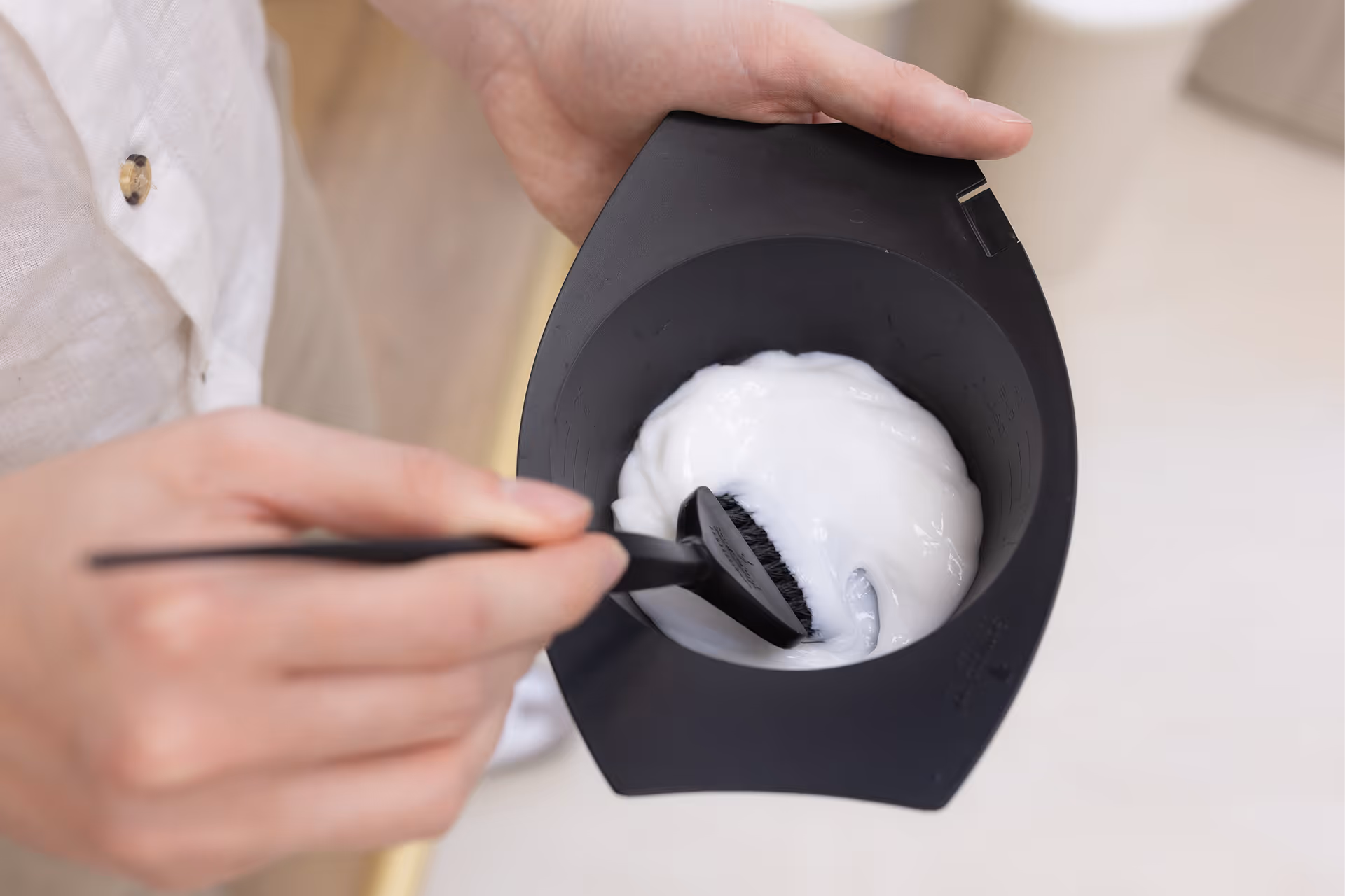 Személy fehér hajfesték krémet kever egy fekete tálban ecset segítségével.