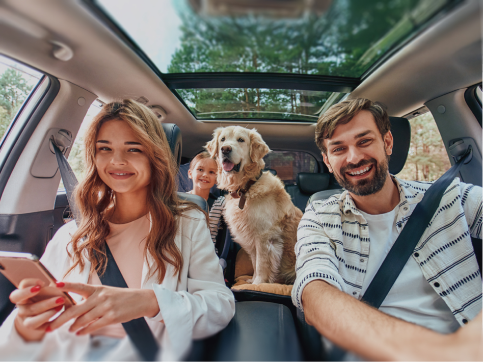 Smiling family of three with a golden retriever inside a car with an open sunroof, enjoying a drive together