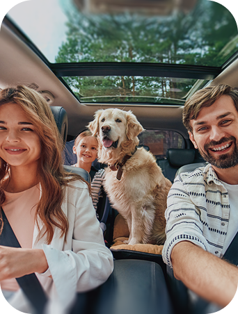 Smiling family with a dog sitting inside a car with a sunroof open during a drive.