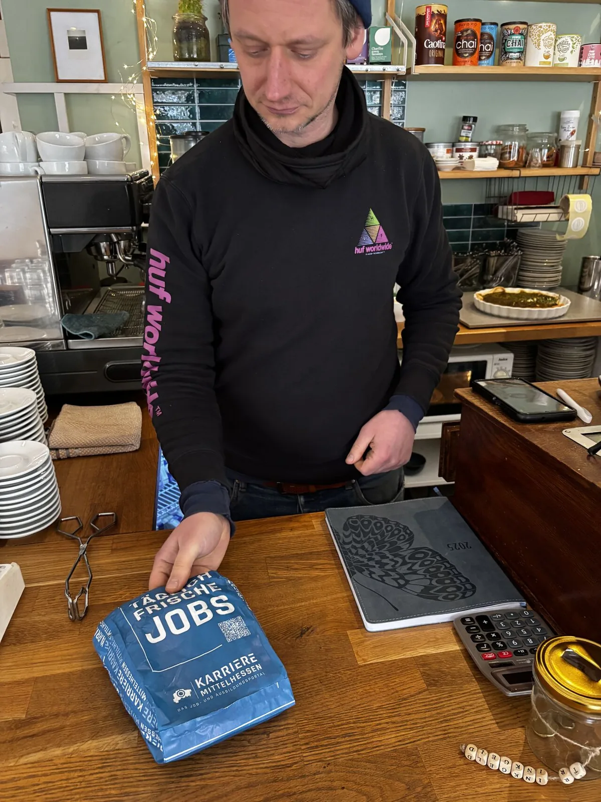 Café-Mitarbeiter am Tresen mit bedruckten Bäckertüten der Karriereportal-Kampagne