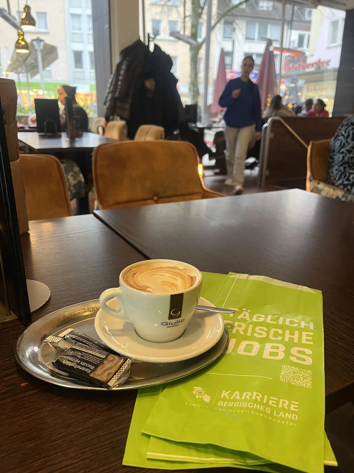 Cappuccino und bedruckte Bäckertüten mit Stellenanzeigen auf einem Cafétisch