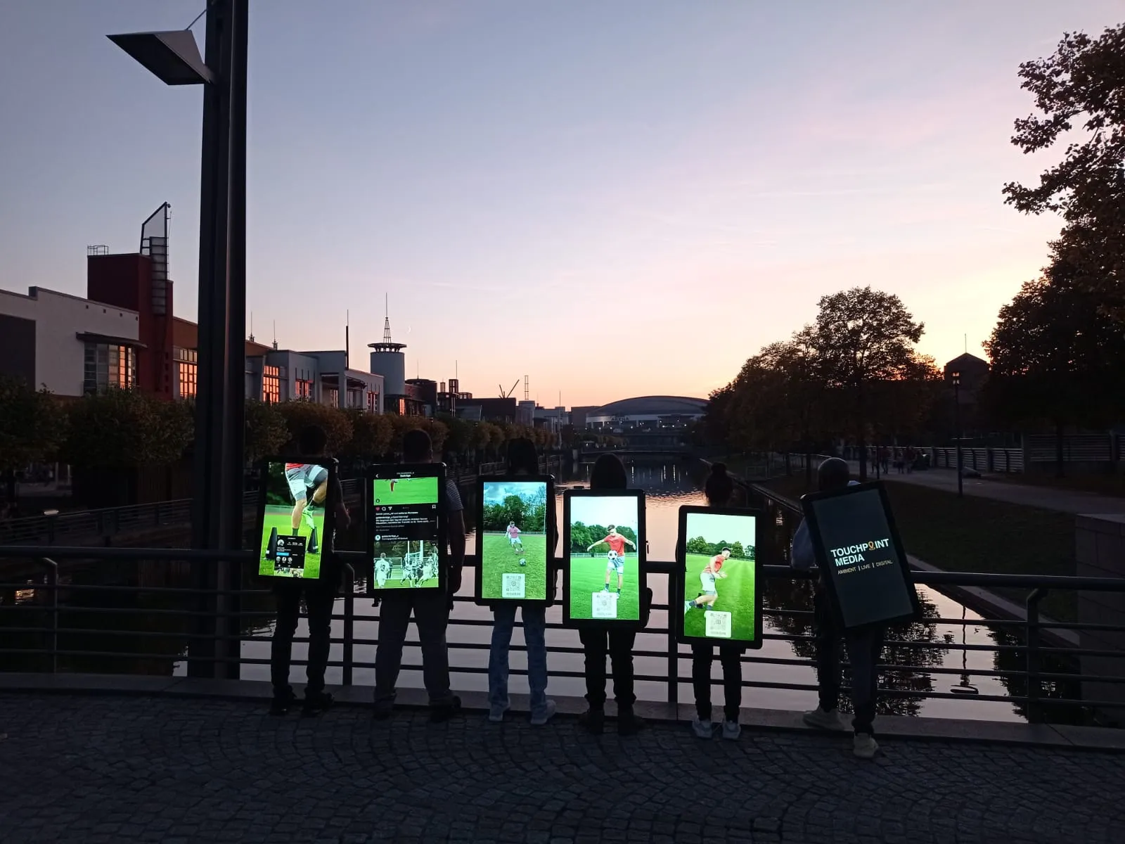 Sechs Promoter mit Walking Screens bei Sonnenuntergang, ein Screen zeigt das Touchpoint Media Branding