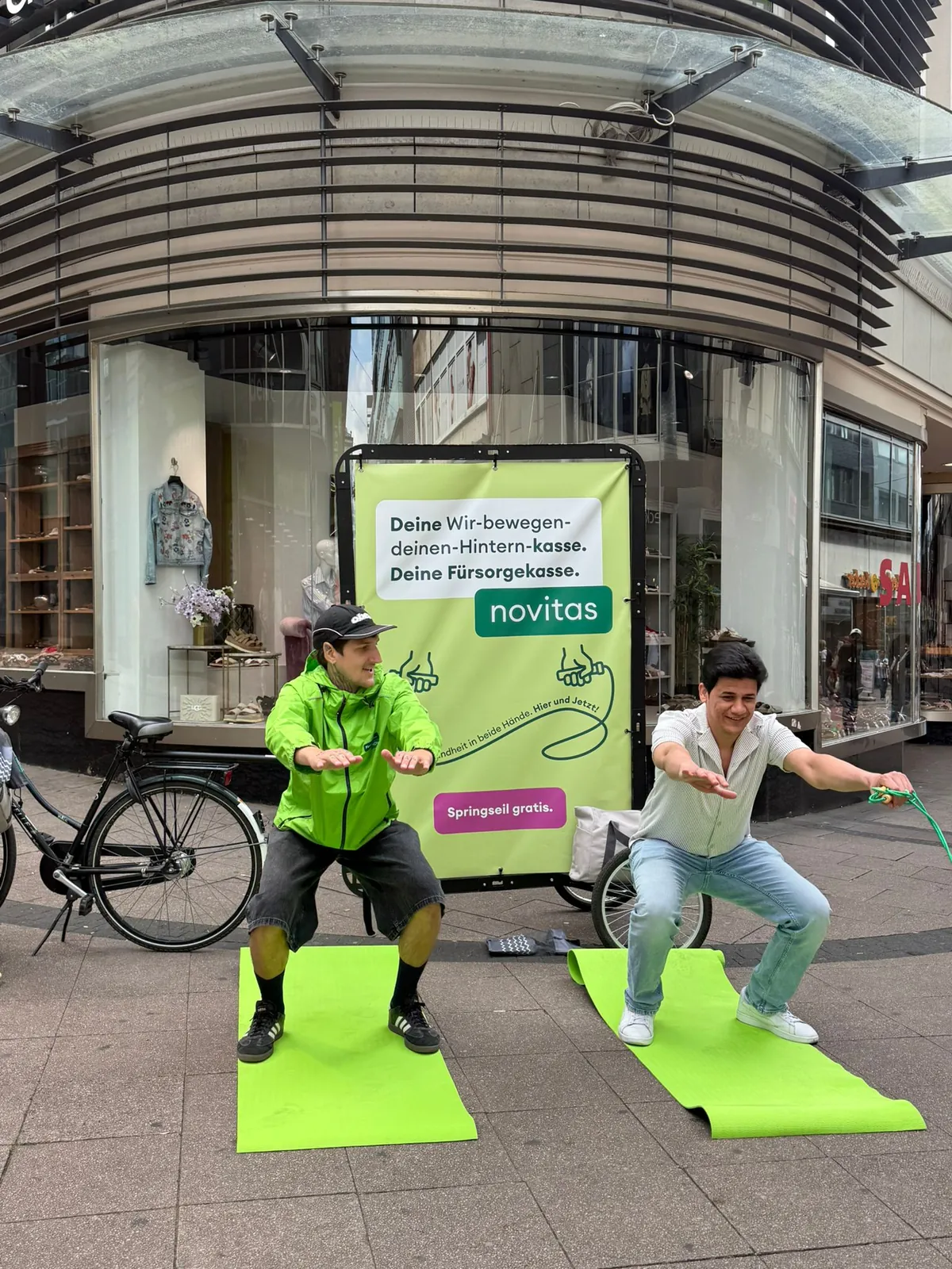 Zwei Promoter machen mit Passanten eine Fitness-Übung auf Matten in der Innenstadt