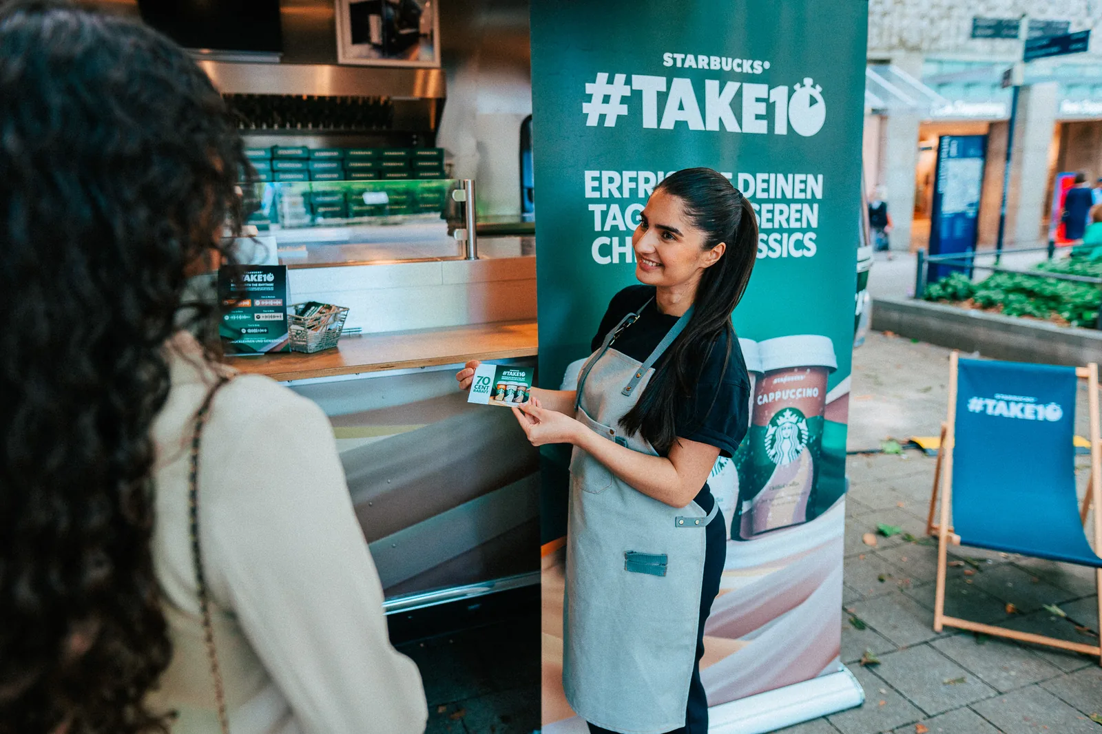 Promoterin am Roadshow-Stand übergibt Produktproben an eine Passantin